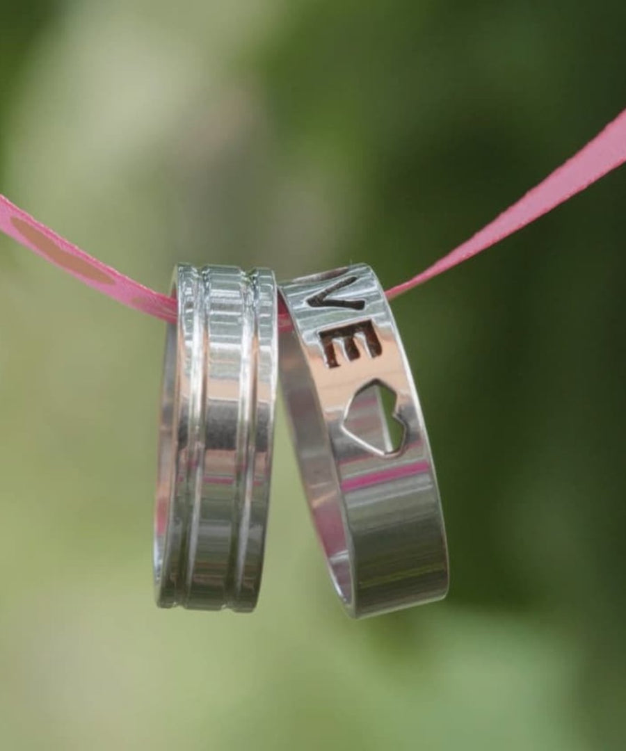 silver love rings hanging on a pink ribbon close-up