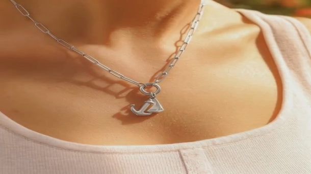 Silver stainless steel charm-holder necklace with anchor and sailboat pendants worn on the neck.